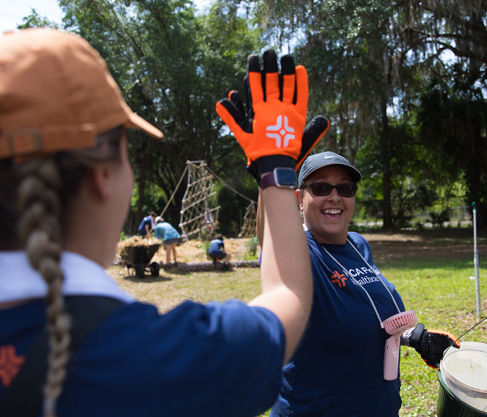 Two colleagues volunteering outside celebrate their teamwork with a high five.